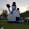 A large Snow Man Bounce House standing in a grassy area, resembling a snow man.