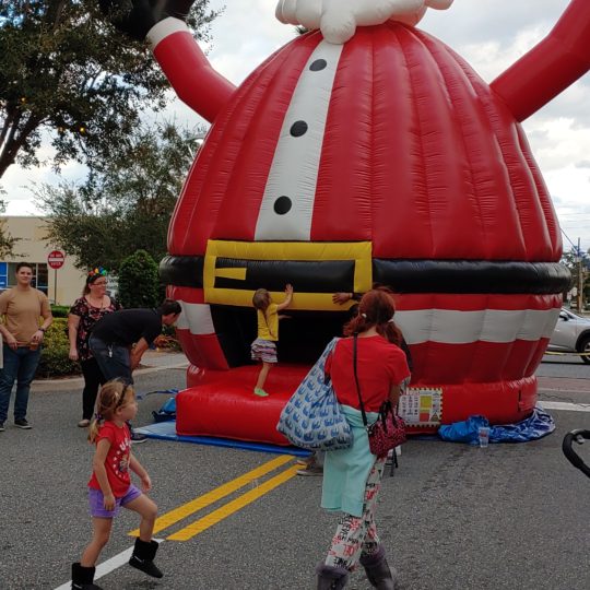 A colossal inflatable Santa Claus Bounce House towering over a bustling street.